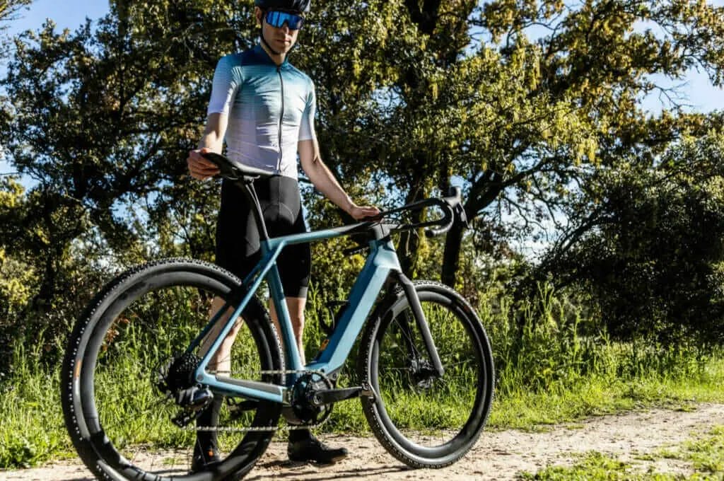 A man is standing next to a bike on a dirt road.