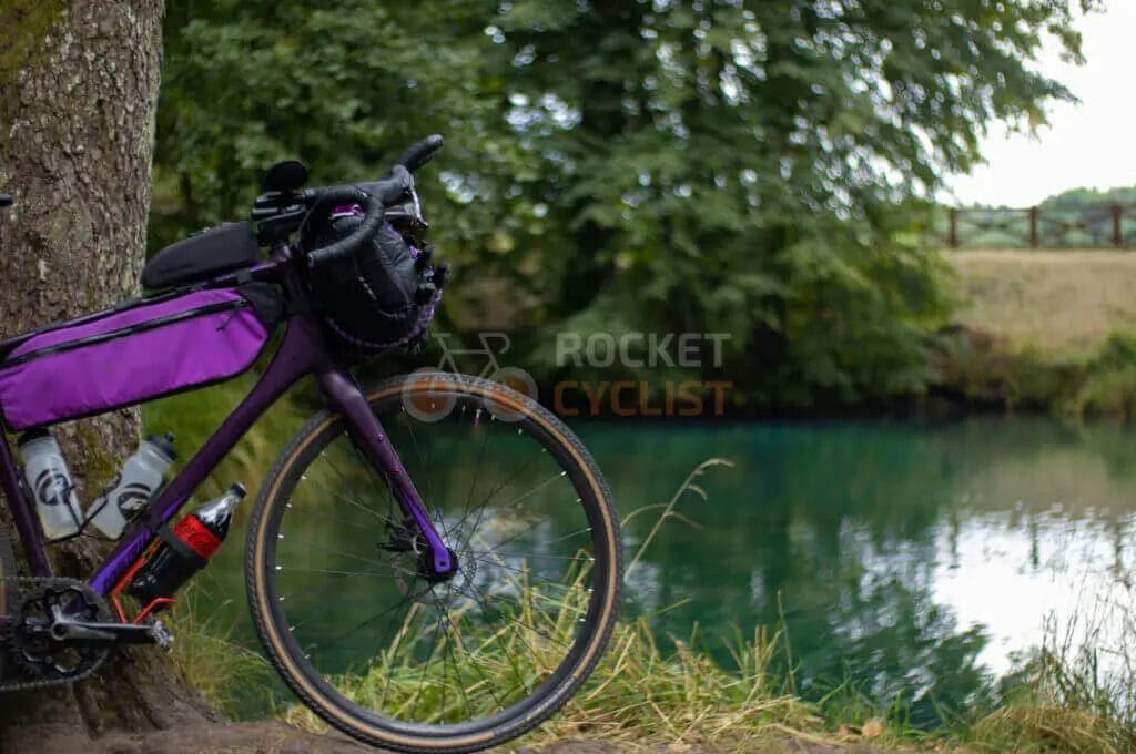 A touring bicycle leaned against a tree by a tranquil riverbank.