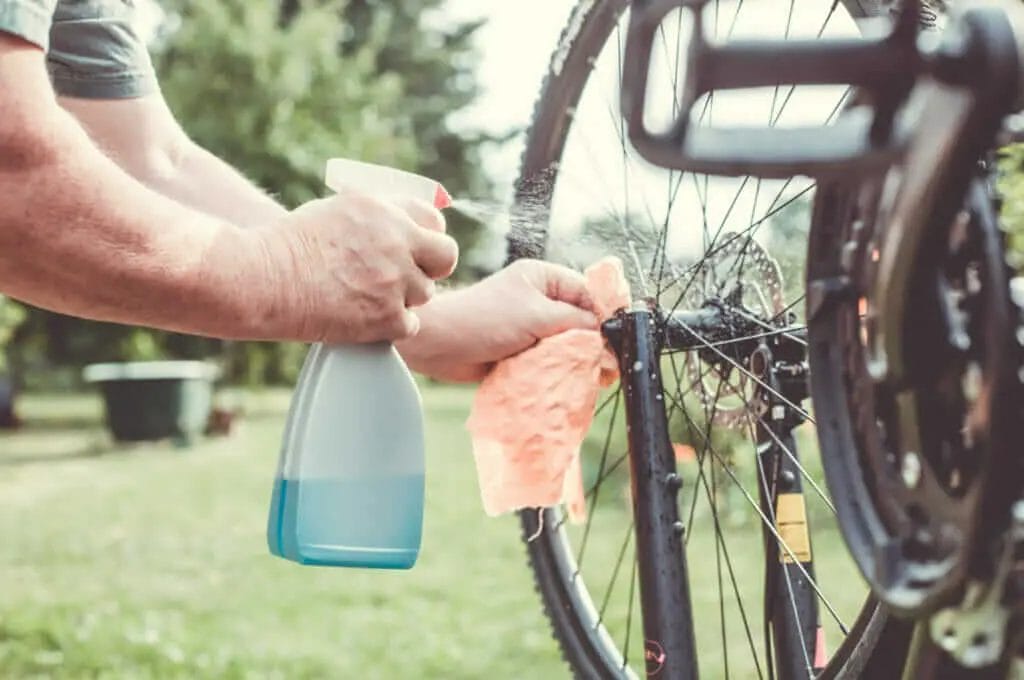 A man cleaning a bicycle wheel with a spray bottle.