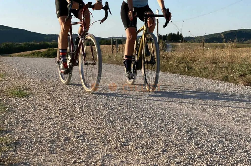 Two people riding bikes down a gravel road.