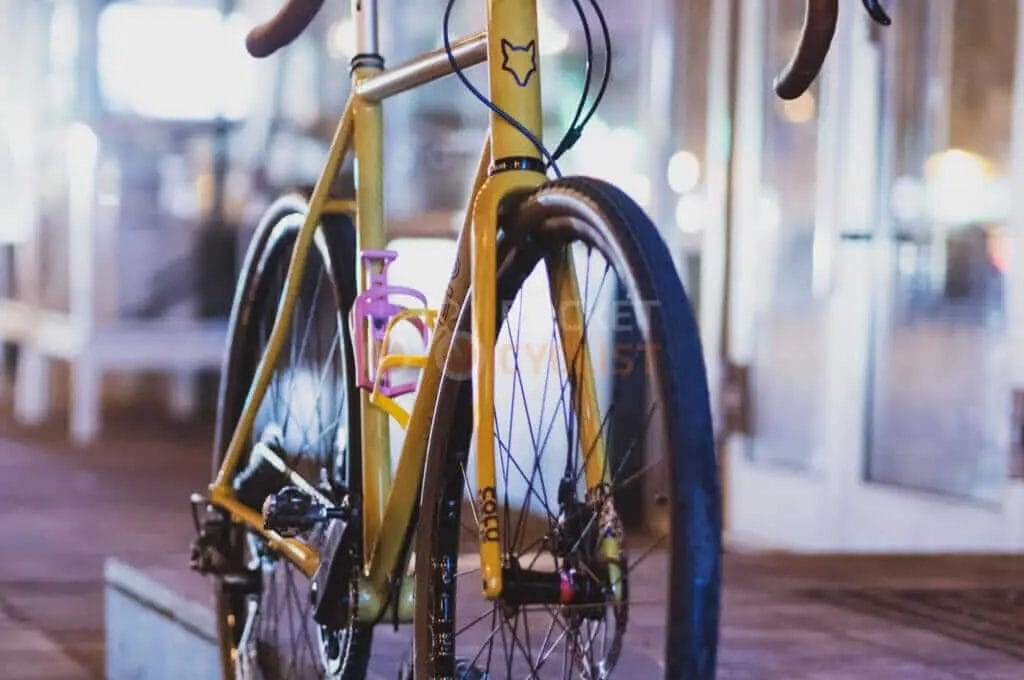 A yellow bicycle is parked on a sidewalk at night.