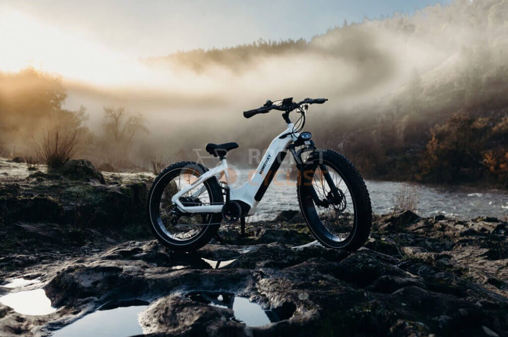 A mountain bike sits on a rocky area near a river.