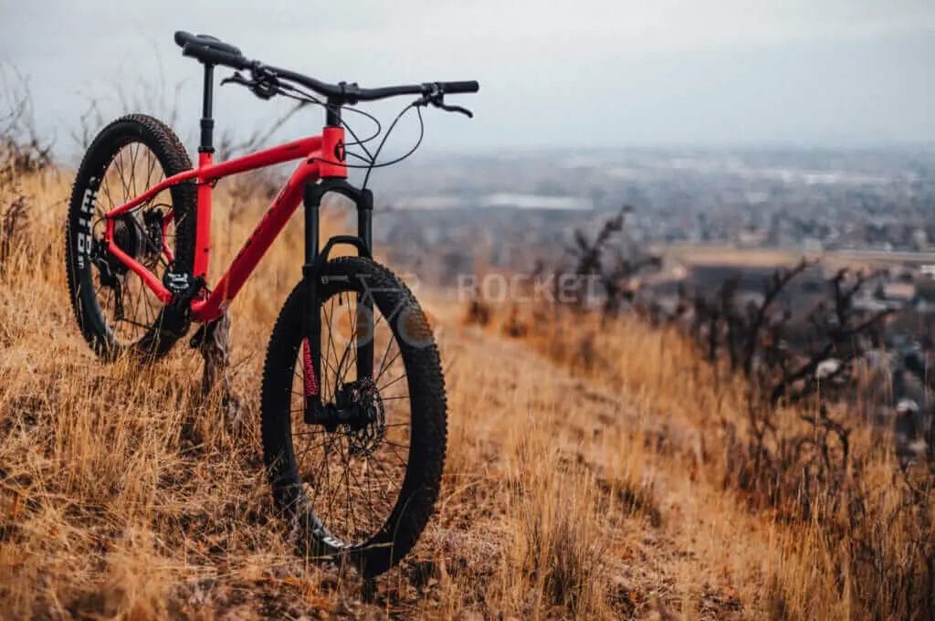 A red mountain bike sits on top of a grassy hill.
