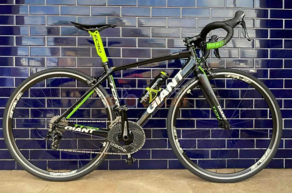 A black and green bike leaning against a blue tiled wall.
