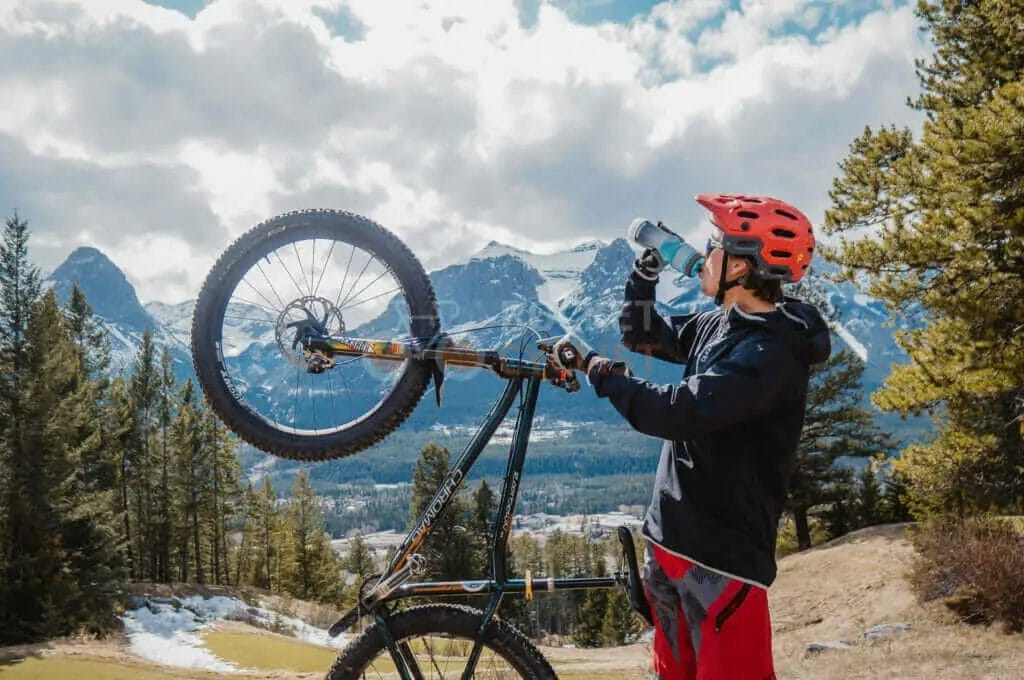 A man holding up a mountain bike in front of mountains.