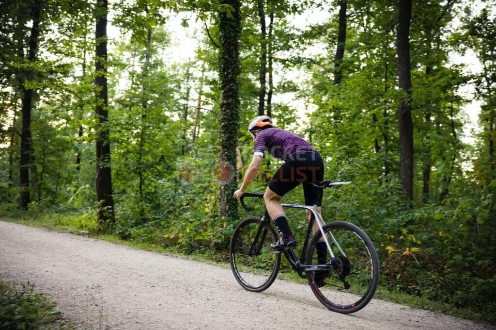 A cyclist riding down a dirt road in the woods.