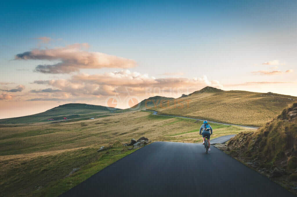A man riding a bike down a mountain road at sunset.