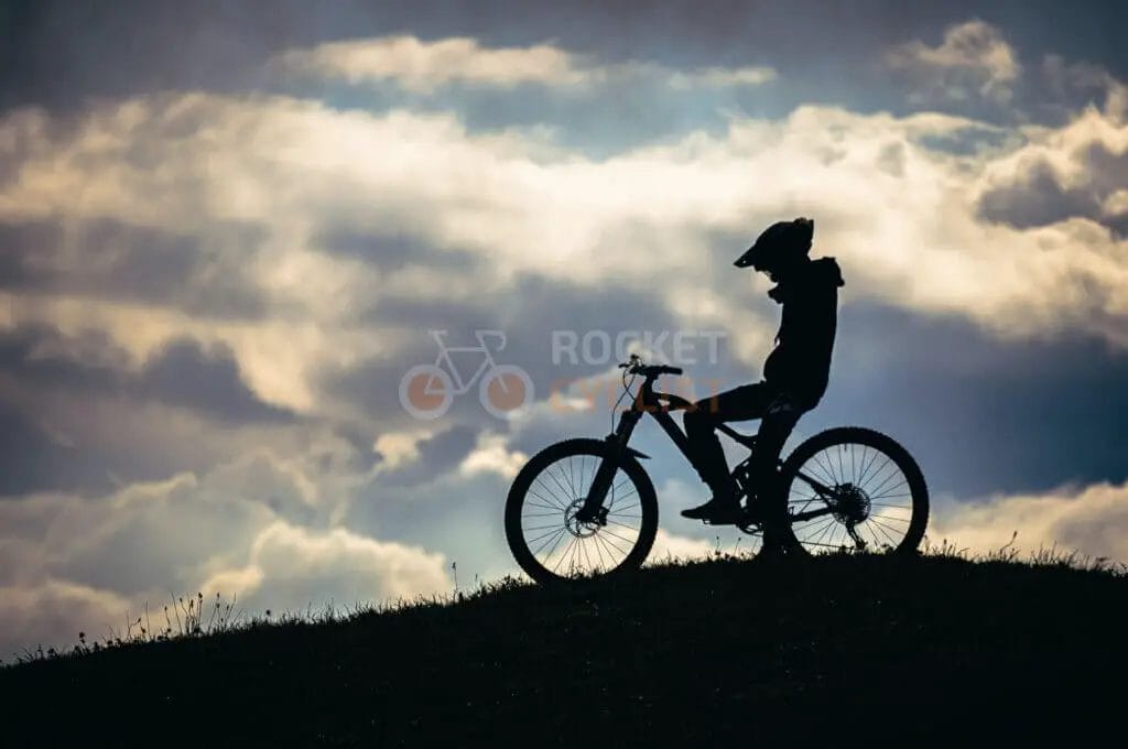 A silhouette of a person riding a mountain bike on a hill.