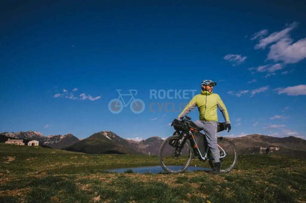 A cyclist standing in front of a mountain with his bike.