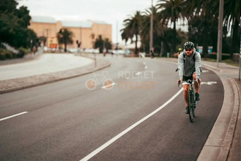 A man riding a bicycle down a street with palm trees.