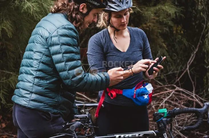 A man and woman looking at a cell phone in the woods.