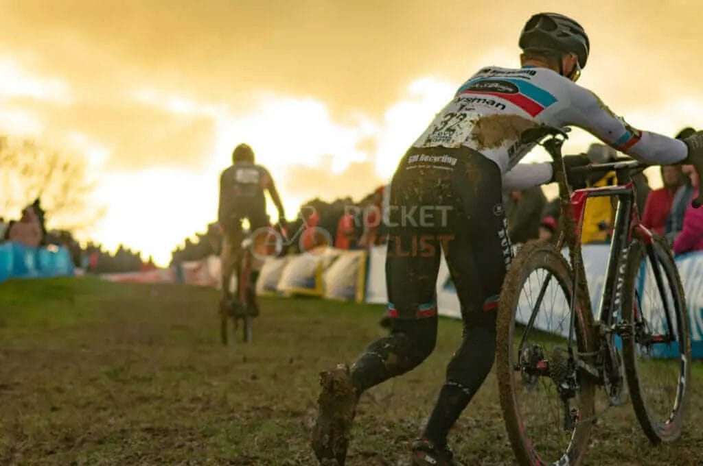 A group of cyclists racing in the mud at sunset.