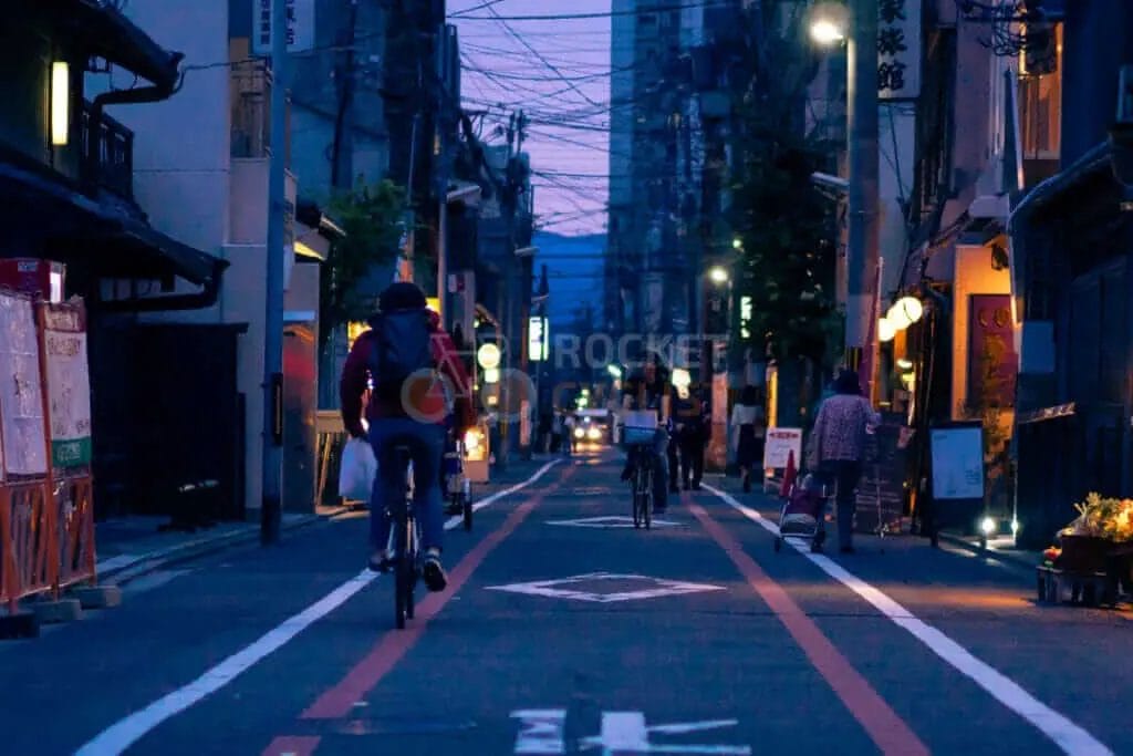 People riding bicycles down a narrow street at night.