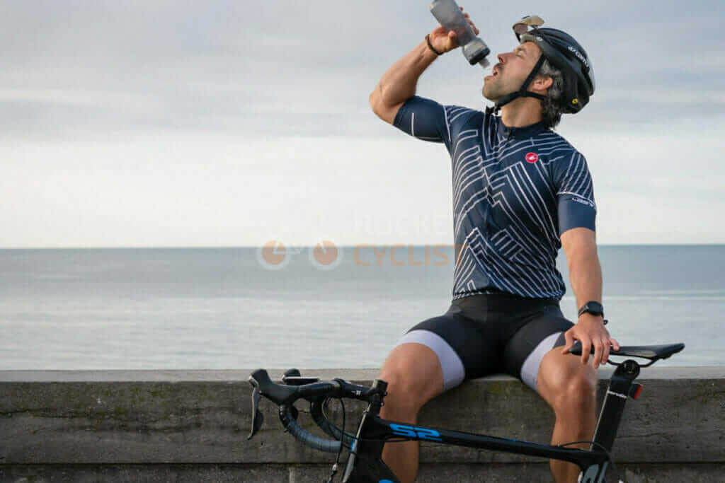 A man drinking from a bottle while sitting on a bike.