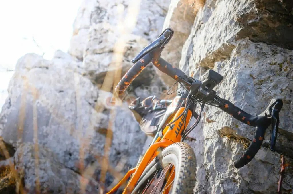 An orange bicycle is leaning against a rock.