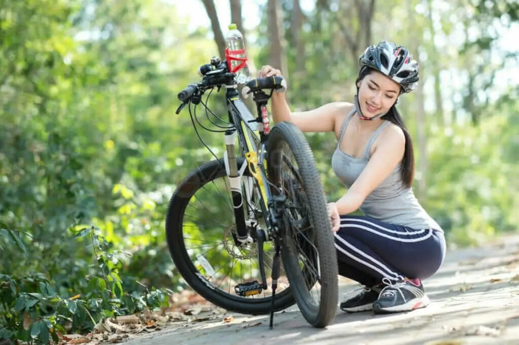 A woman fixing her bicycle in the woods.