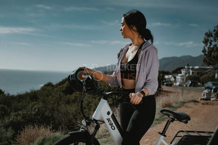 A woman riding an electric bike on a hill overlooking the ocean.