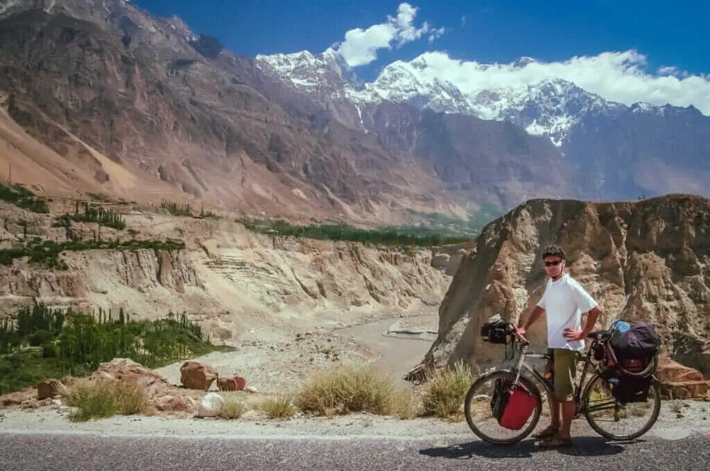 A man standing next to his bike in front of mountains.