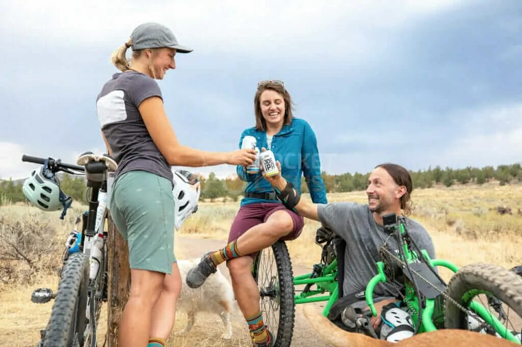 A group of people sitting on a bike with a bottle of beer.