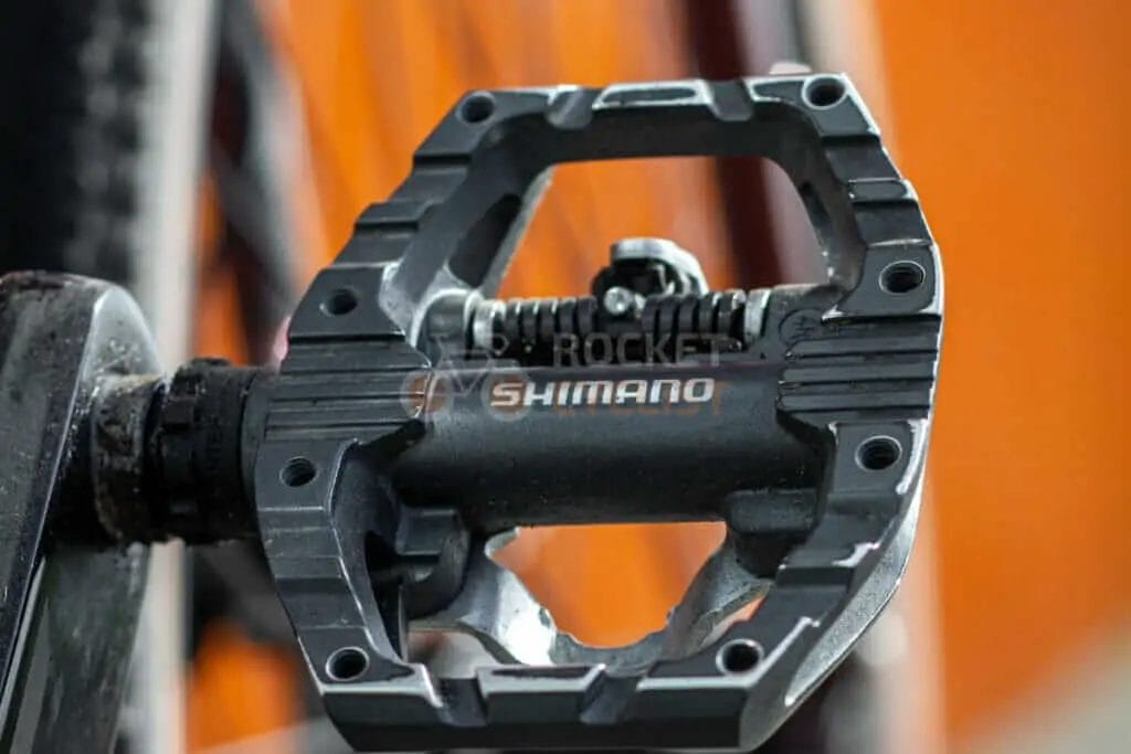 A close up of a bicycle pedal with an orange background.