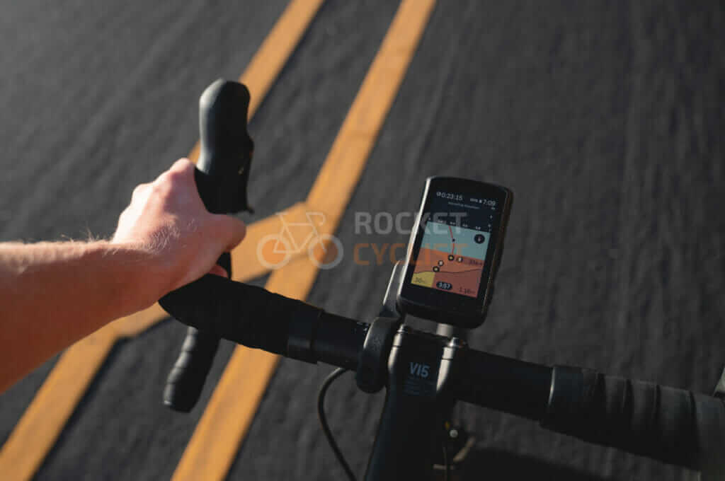 A person's hand is holding a phone on the handlebars of a bicycle.