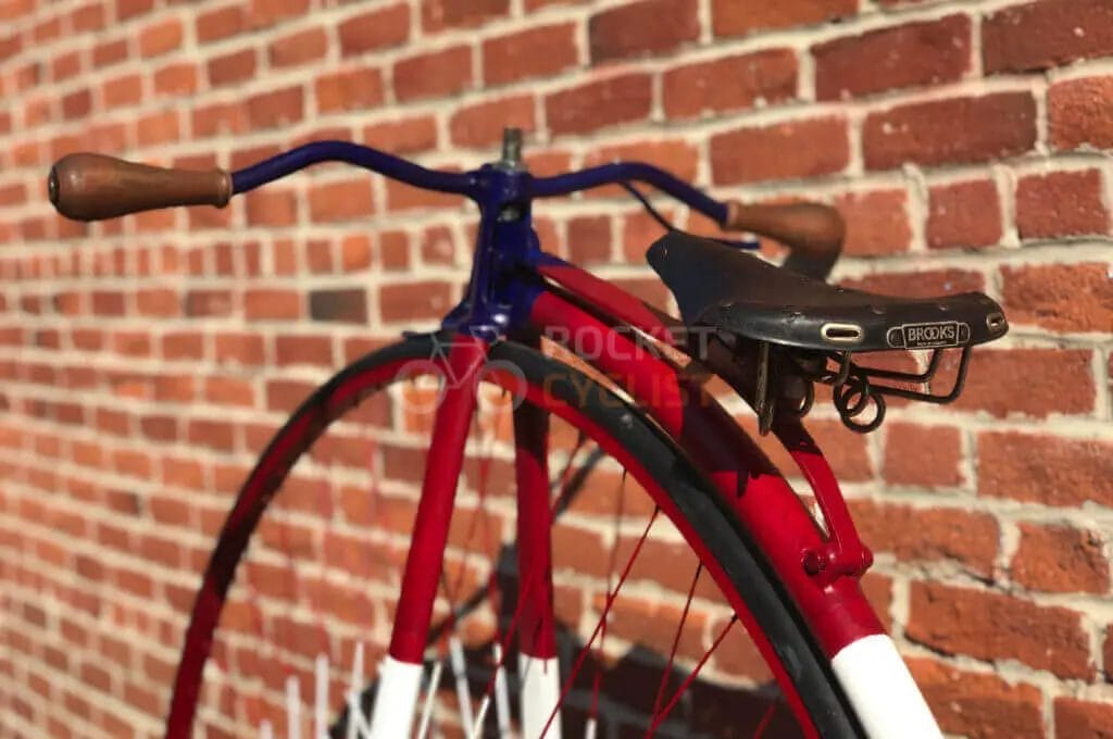 A red, white and blue bicycle leaning against a brick wall.