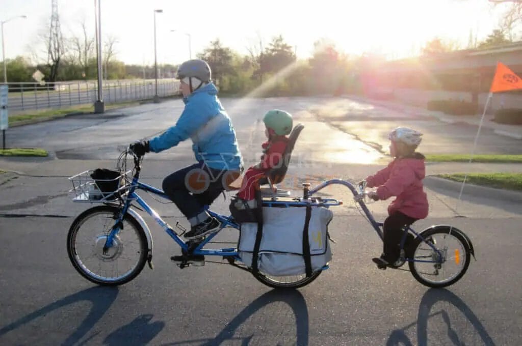 A man and a woman riding a bike with a child in a basket.