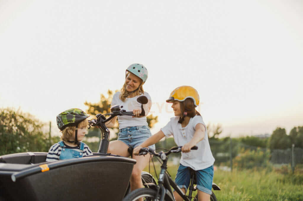 A mother and her two children are riding bikes in a trailer.