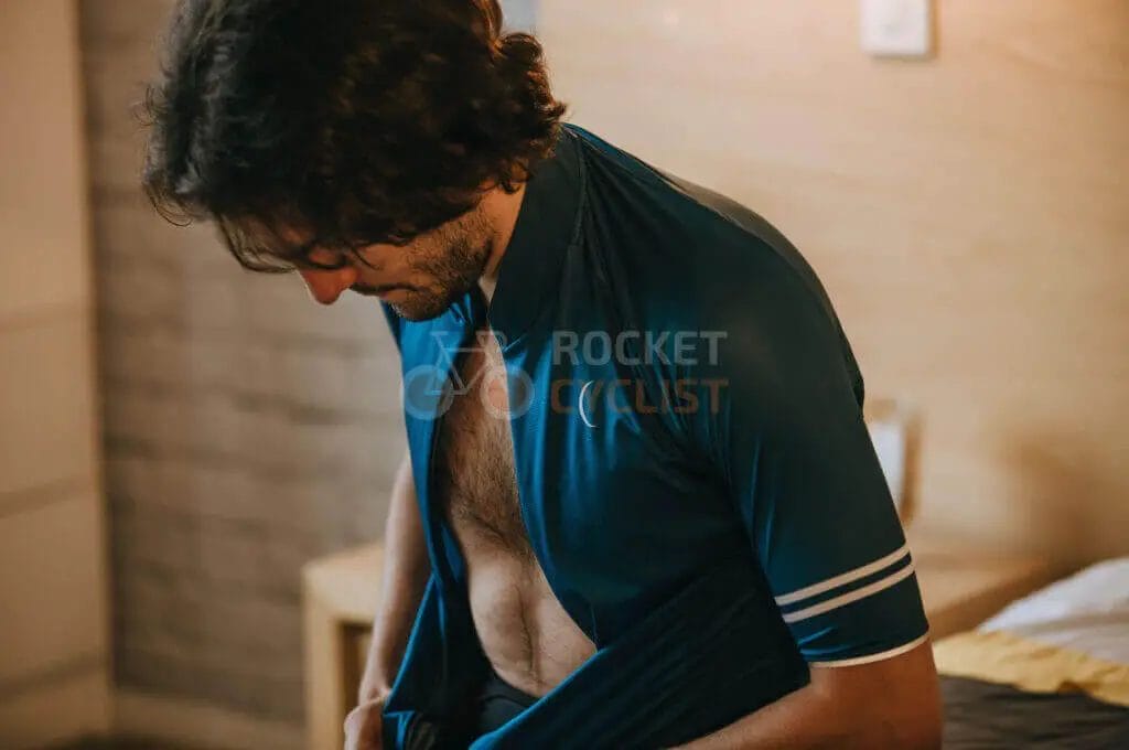 A man putting on a shirt in a hotel room.