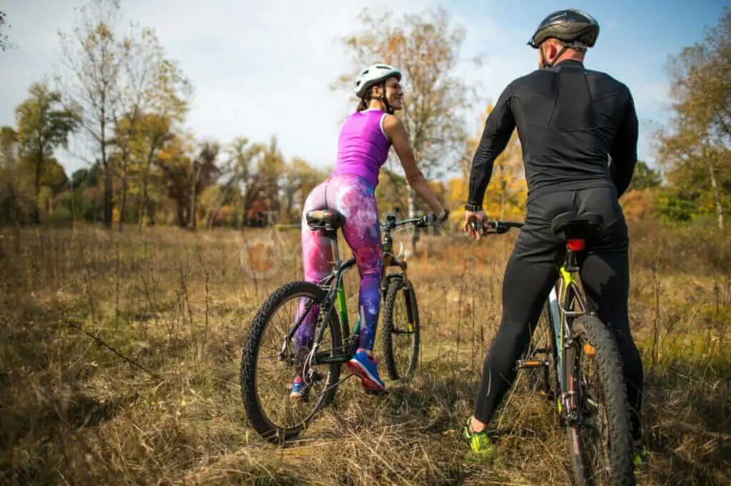 A man and woman are riding their bicycles in a field.