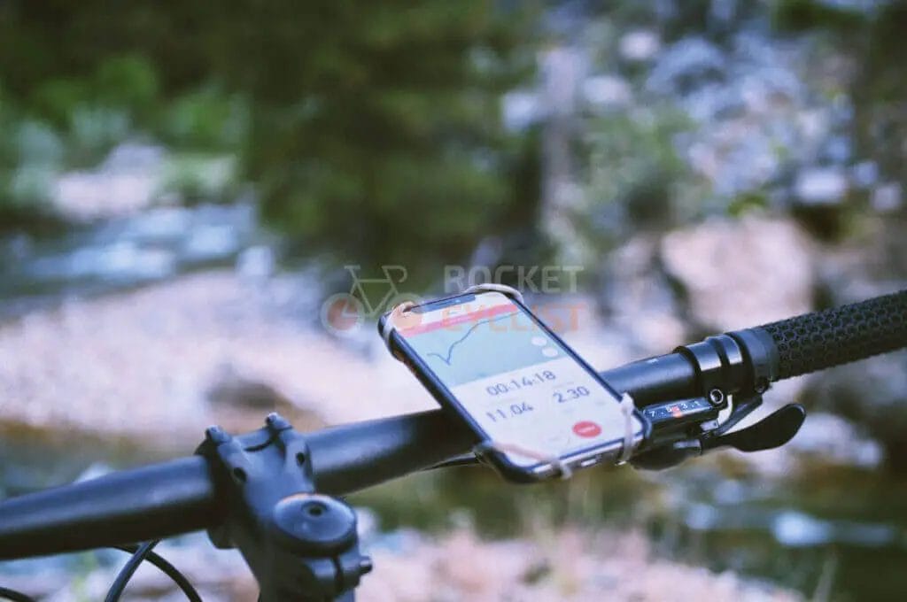 A bicycle with a cell phone attached to the handlebar.