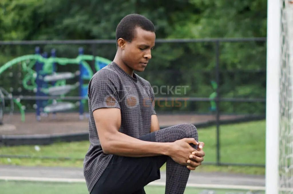 A young man stretching his leg on a soccer field.