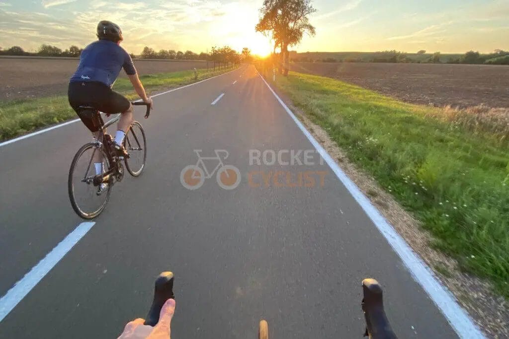 Two people riding bikes on a country road at sunset.