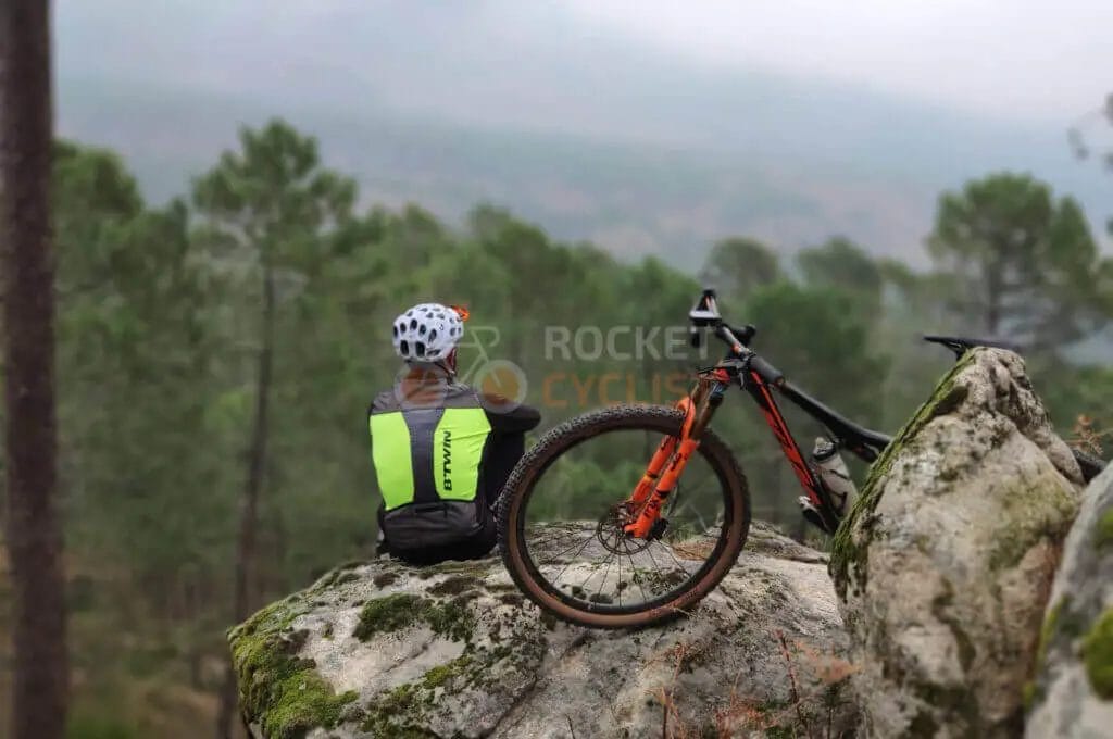 A woman sits on a rock with her mountain bike.