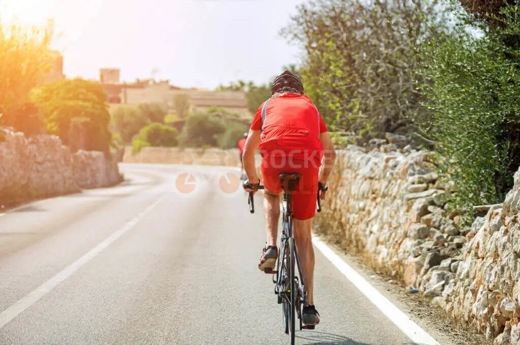A cyclist riding down a road with a stone wall in the background.