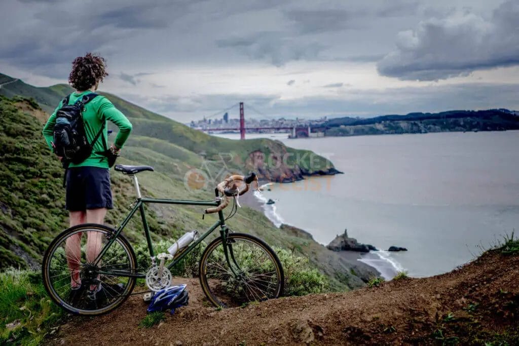A man with a bike on a hill overlooking the ocean.