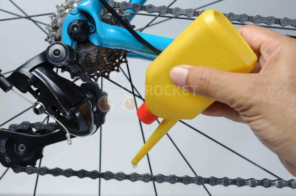 Lubricating a bicycle chain with oil from a yellow squeeze bottle.
