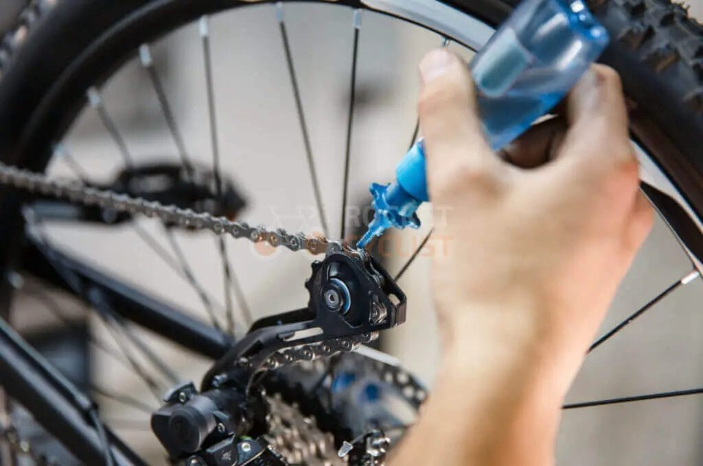 A person fixing a bicycle chain with a bottle of water.