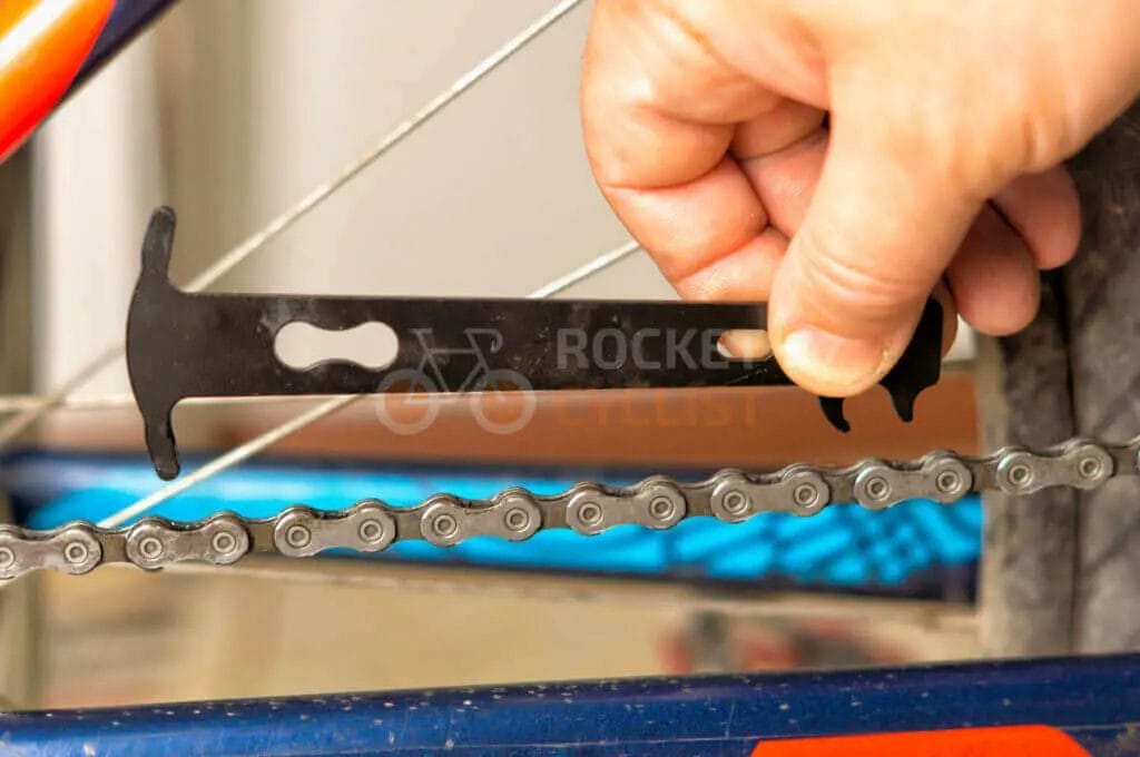 A person aligning a bicycle chain checker tool on a bike chain to assess wear.