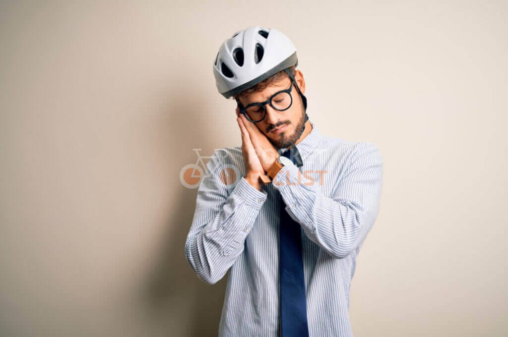 A man in a bicycle helmet with eyes closed and hands pressed together as if in thought or sleepiness.