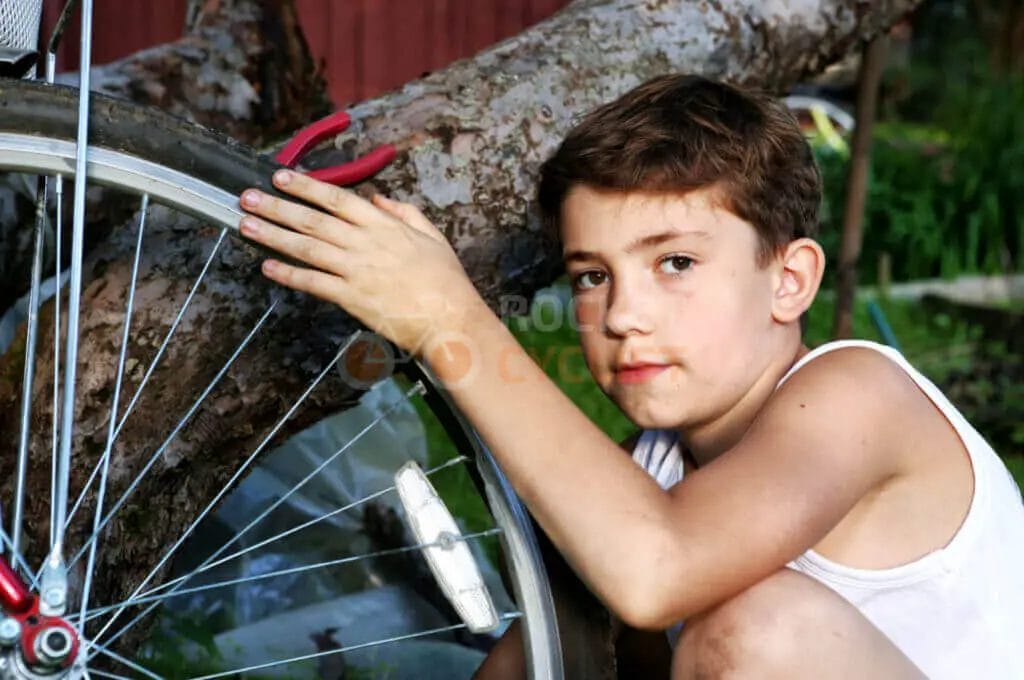 A young boy leaning against a tree with a bicycle wheel.