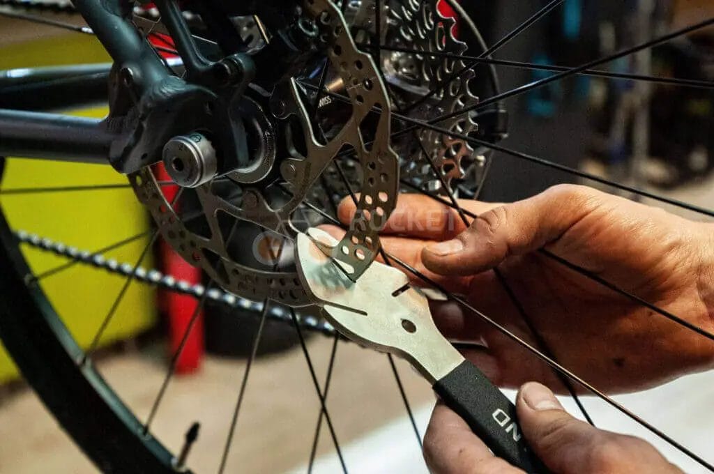 A person is working on a bicycle wheel with a pair of pliers.