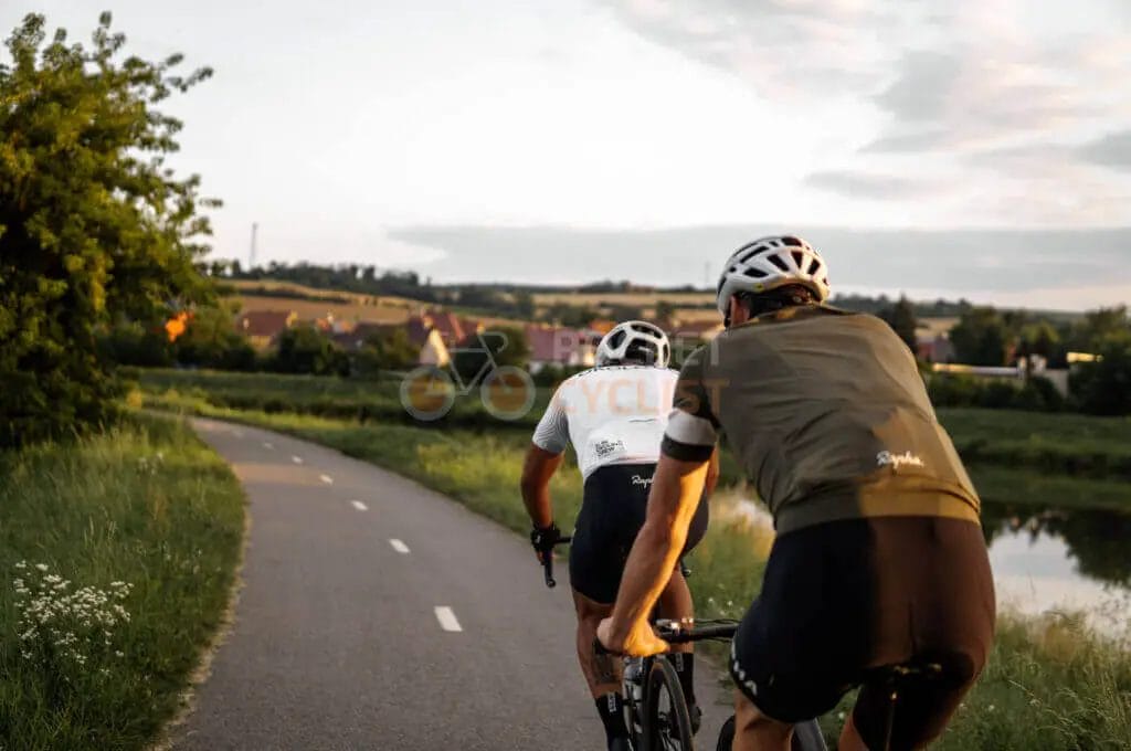 Two cyclists riding bikes on a paved path near a river.