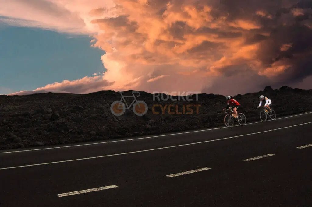 Two cyclists riding on a road under a cloudy sky.
