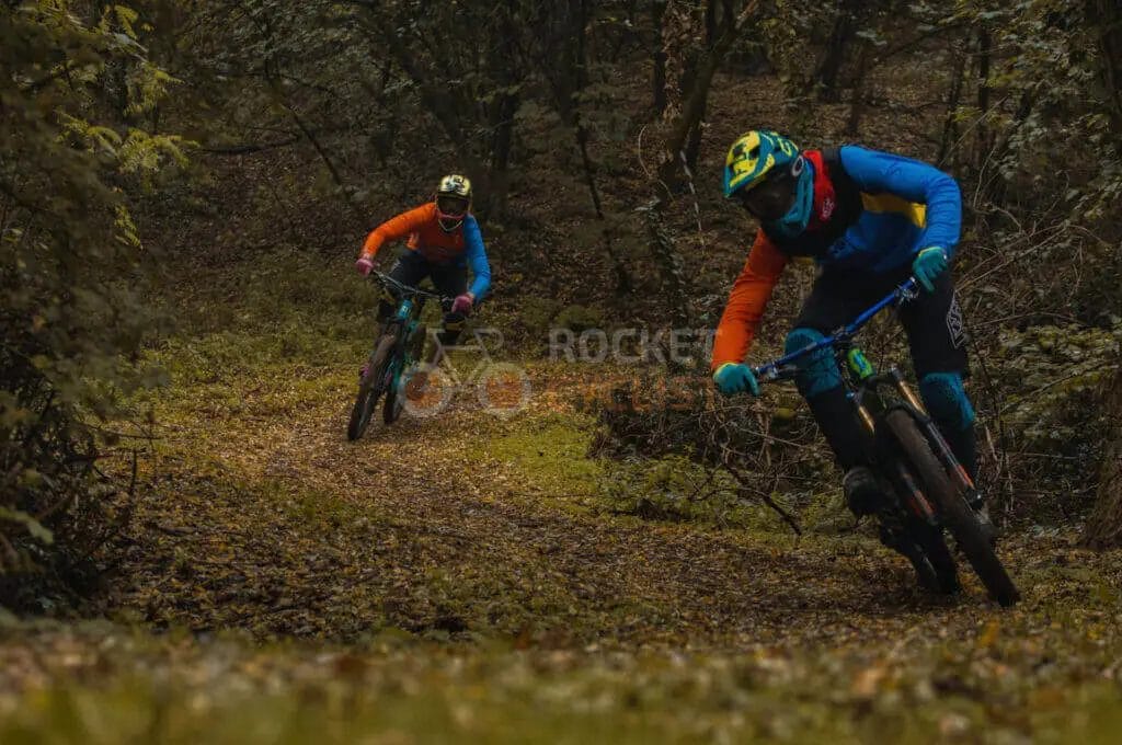 Two mountain bikers riding down a trail in the woods.
