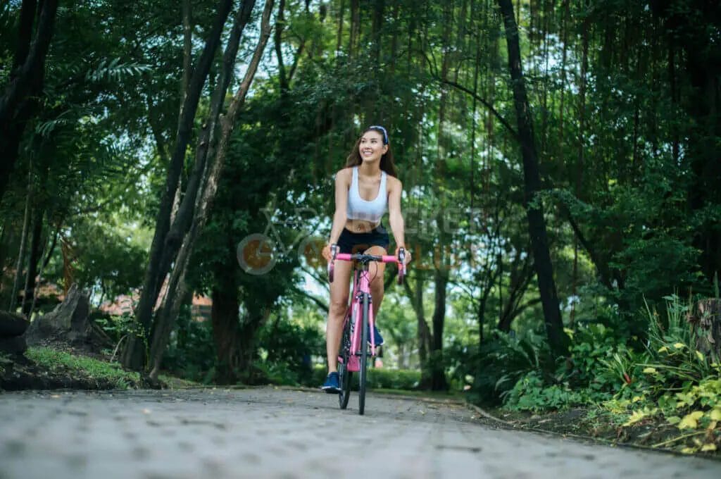 A young woman riding a pink bicycle in the woods.