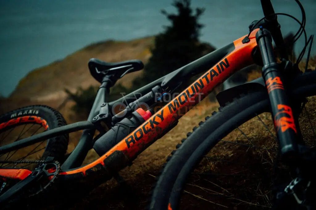 An orange and black mountain bike leaning against a hill.