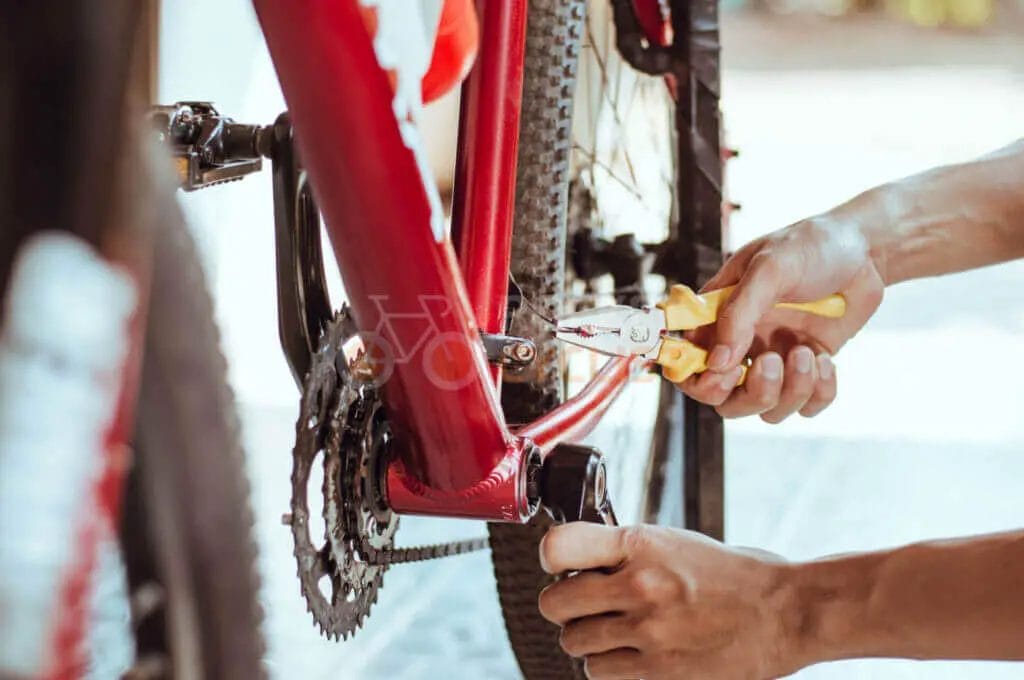 A man is working on a bicycle with pliers.