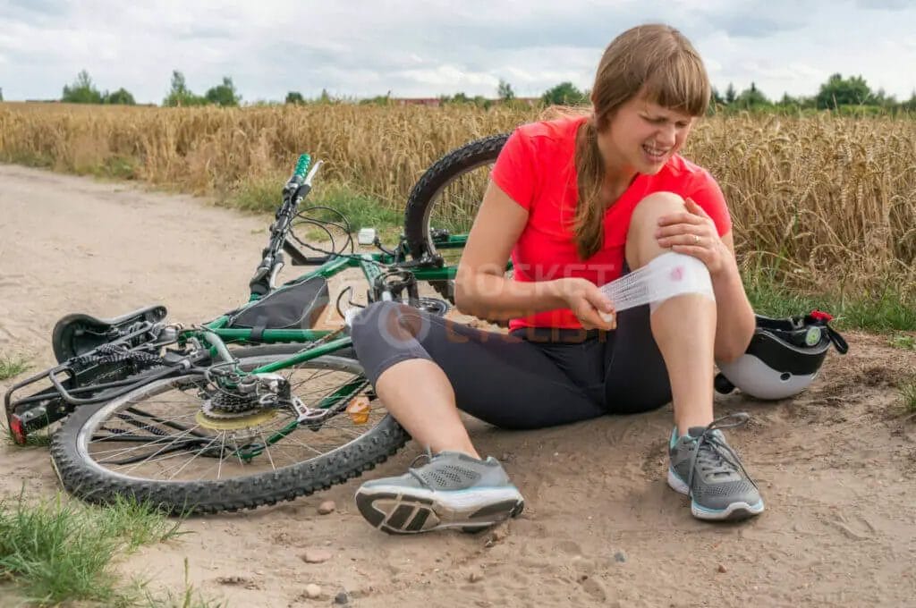A woman sitting on the ground next to her bicycle with a bandage on her knee.