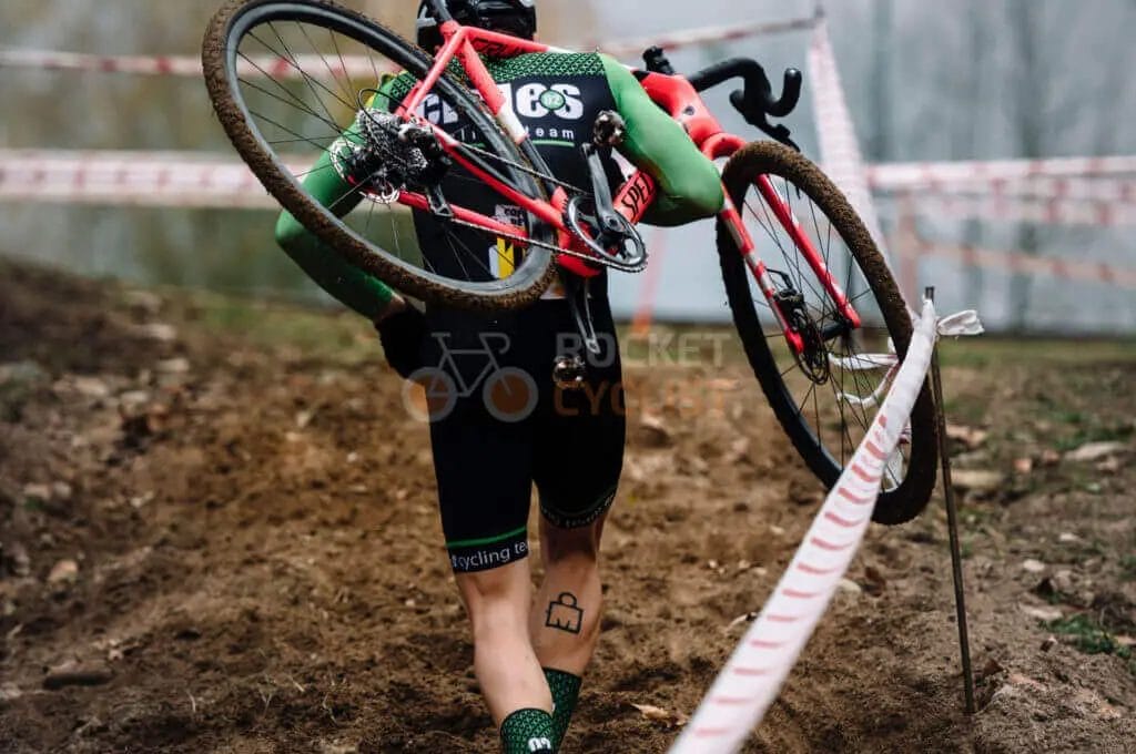 A cyclist carrying his bike over a muddy trail.